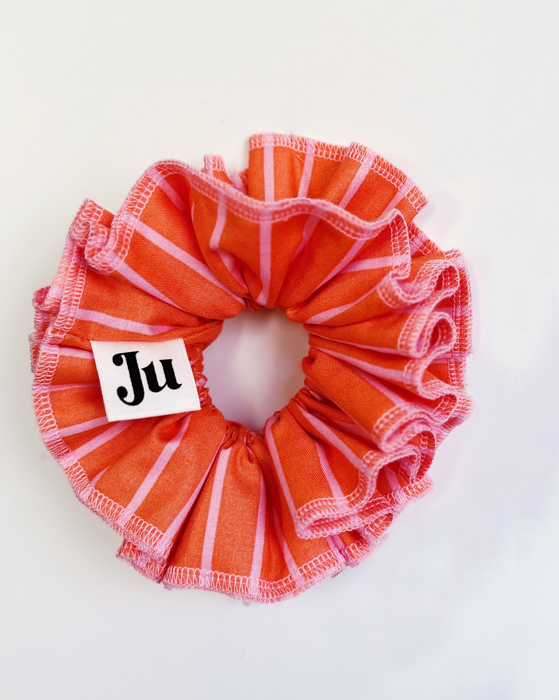 A handmade orange and pink striped cotton scrunchie with contrast pink stitching, displayed on a white background.