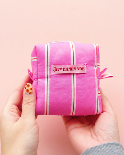 a boxy shape zipper pouch in pink striped fabric with "theJU" pink woven label