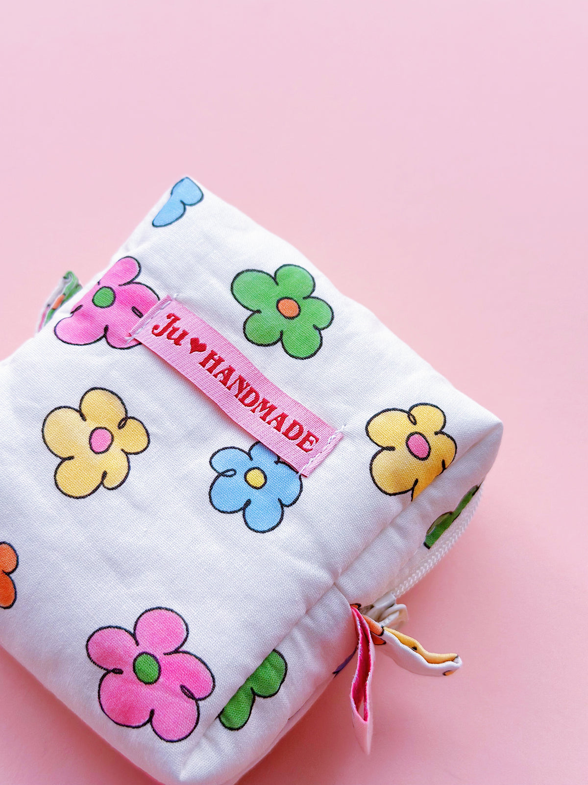 a cute colorful daisy zip up make up bag with "theJU" pink woven label