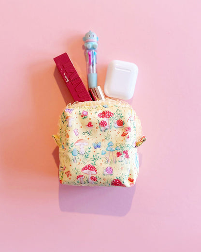 Handmade fairy tale mushroom print quilted zipper pouch with ruffled lace trim, boxy 10×10×5cm design on a pink background.
