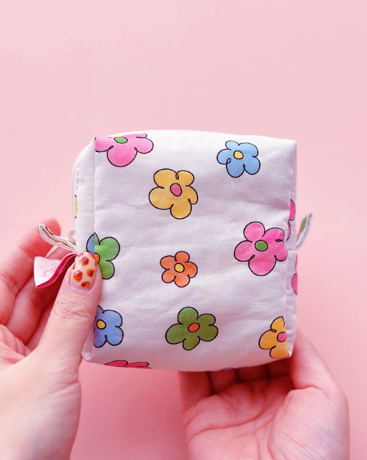 a cute colorful daisy zip up make up bag in a pink background
