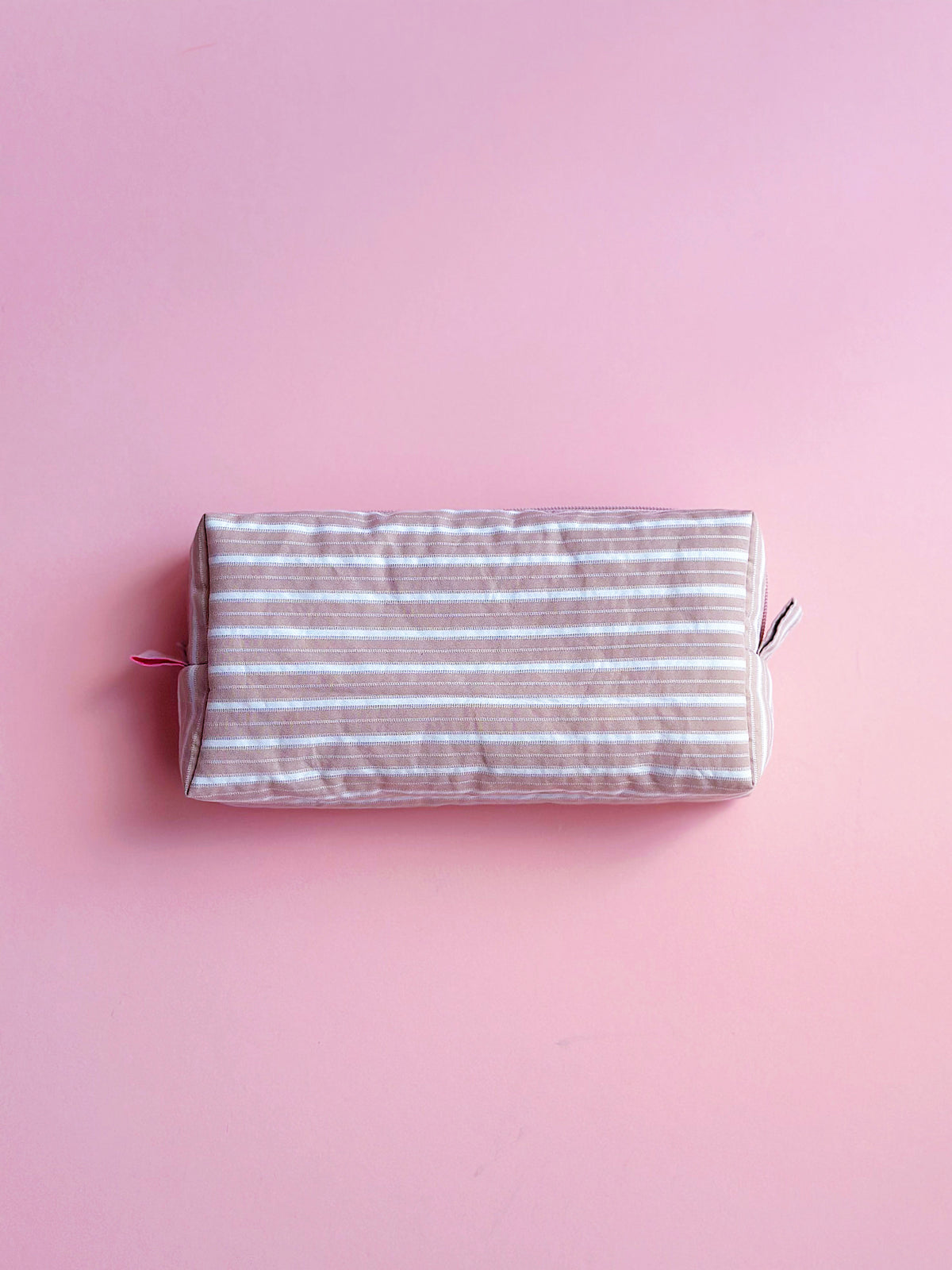 a back view of pastel brown striped zip pouch for make up and camera 
