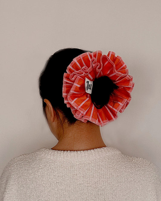 A handmade orange and pink striped cotton scrunchie with contrast pink stitching.