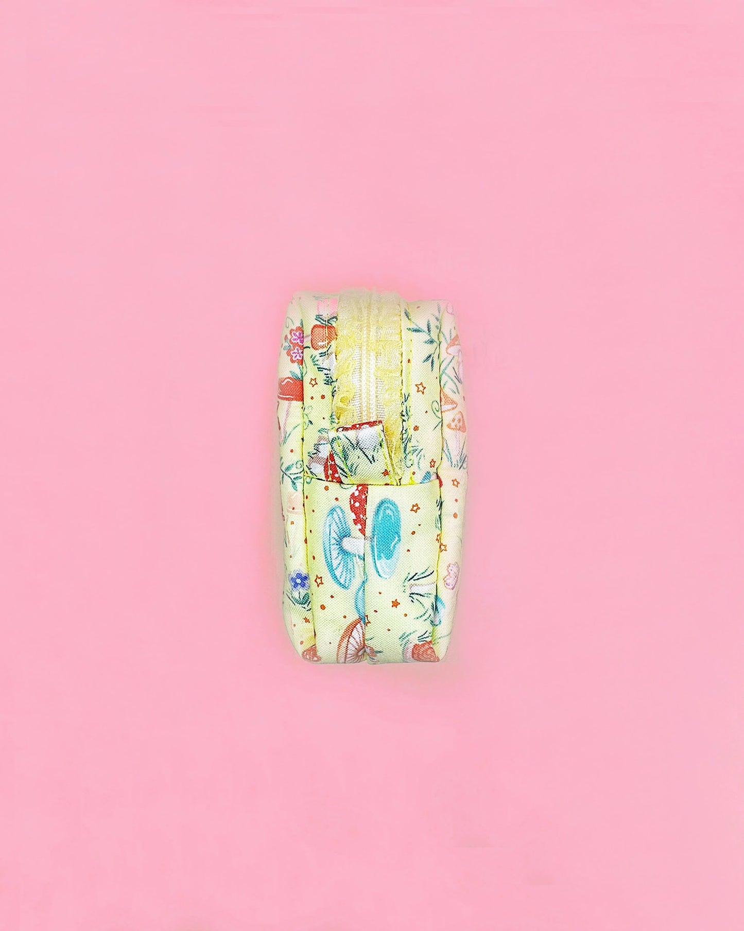 Handmade fairy tale mushroom print quilted zipper pouch with ruffled lace trim, boxy 10×10×5cm design on a pink background.