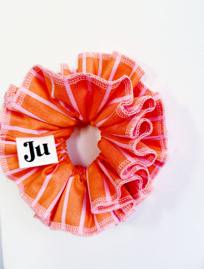 A handmade orange and pink striped cotton scrunchie with contrast pink stitching, displayed on a white background.