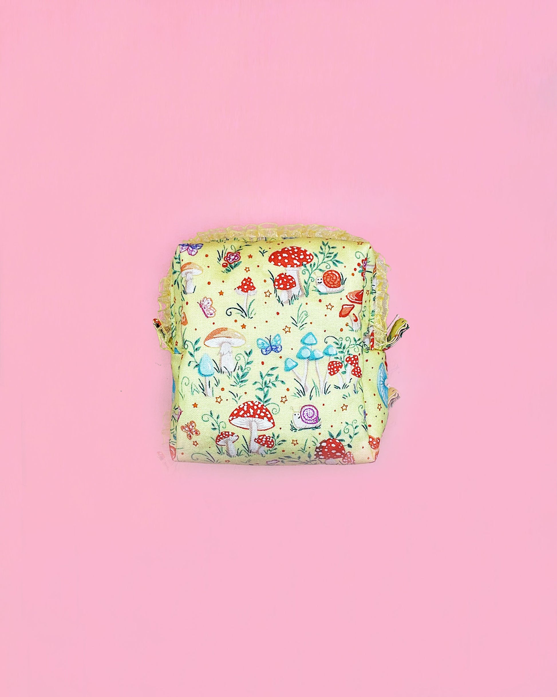Handmade fairy tale mushroom print quilted zipper pouch with ruffled lace trim, boxy 10×10×5cm design on a pink background.