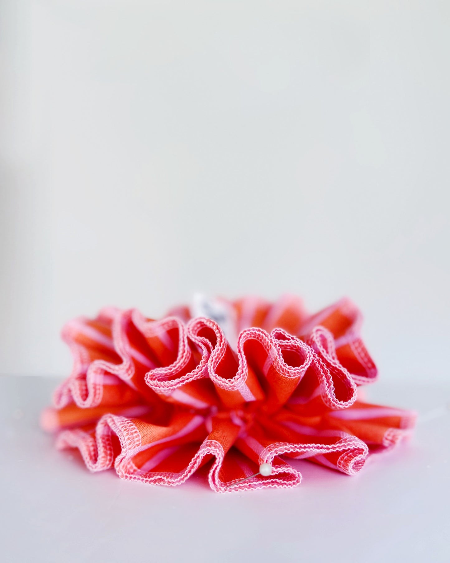 A handmade orange and pink striped cotton scrunchie with contrast pink stitching, displayed on a white background.
