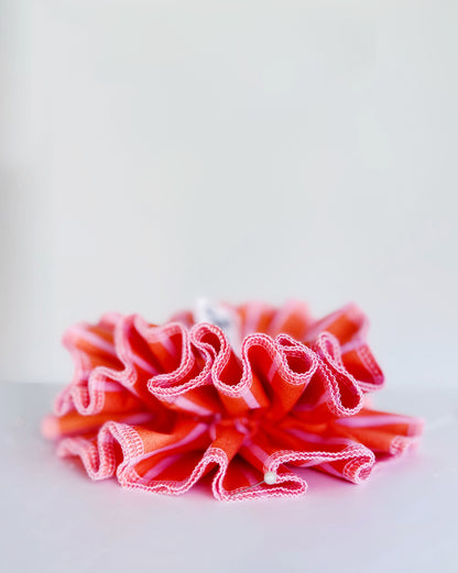 A handmade orange and pink striped cotton scrunchie with contrast pink stitching, displayed on a white background.